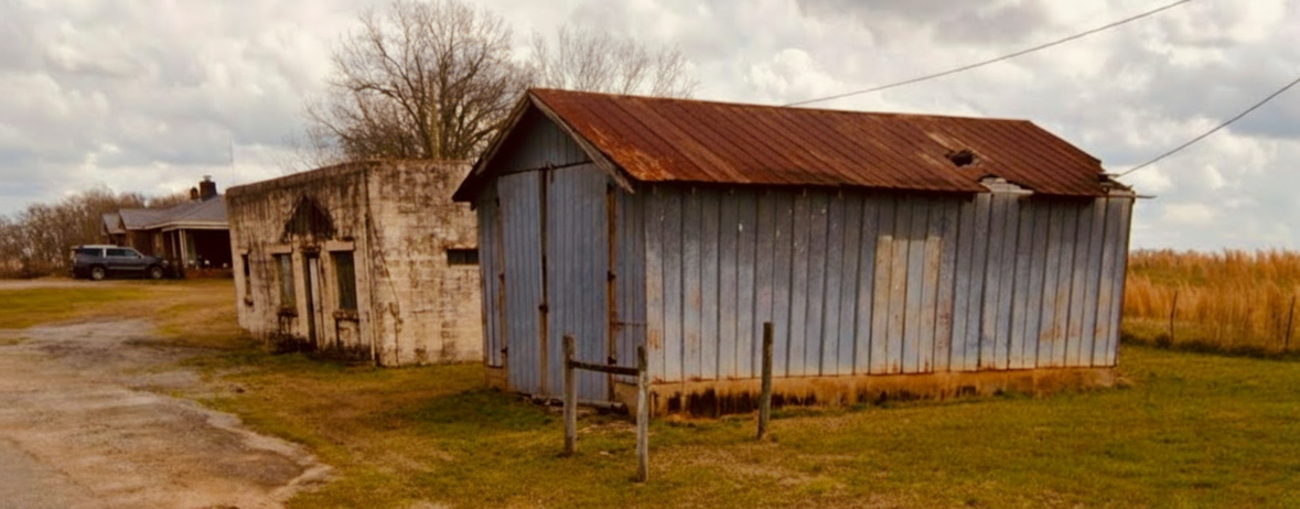 A weathered tin-roofed shop building on the Home Place, standing at the edge of an open field under a pale sky