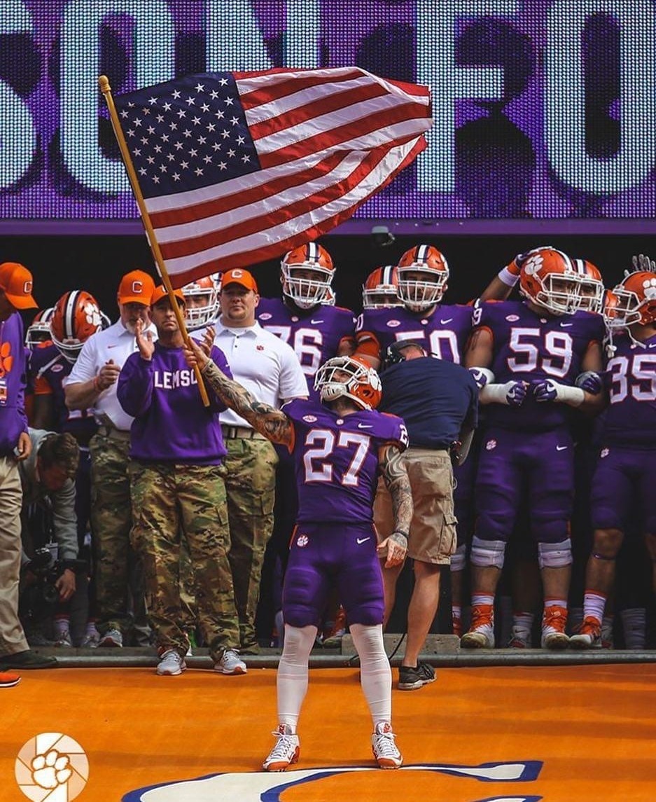 Johnathan Alexander Dalton in a Clemson football uniform carrying the American flag while running down The Hill into a packed stadium