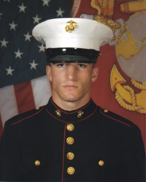 Studio portrait of Johnathan Alexander Dalton as a young Marine in dress blues with a white cover, photographed against a United States flag and a Marine Corps flag