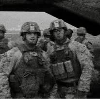 Grainy black and white photograph of several Marines in helmets and body armor standing close together in the open