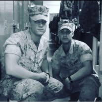 Black and white photograph of two Marines in camouflage utilities and caps crouching in front of a row of wall lockers